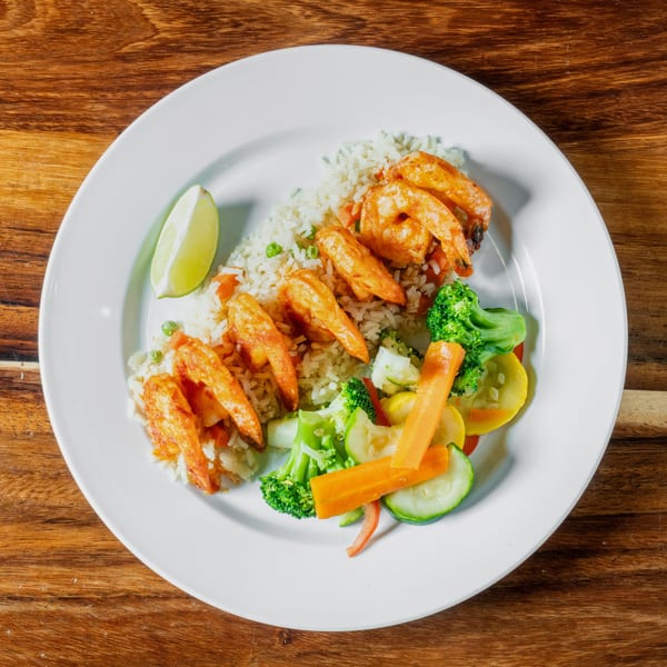 Grilled shrimp with rice, mixed vegetables, and a lime wedge on a white plate.