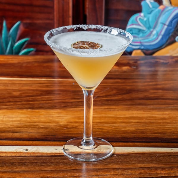 Margarita in a martini glass with a salted rim and a dried lime slice on a wooden table.
