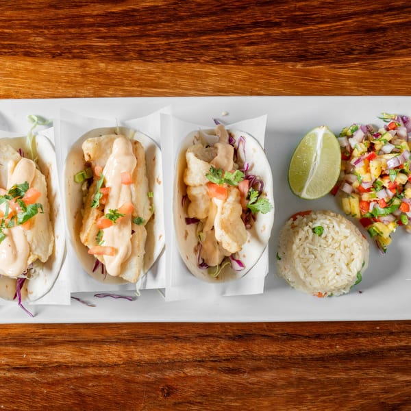 Three fish tacos with sauce, cilantro, and tomatoes, served with rice, salsa, and lime.