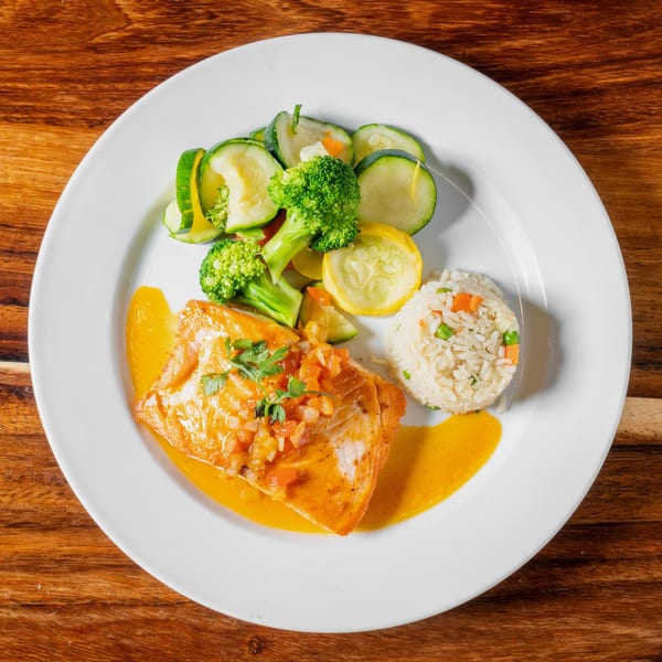 Salmon fillet with tomato salsa, rice, and steamed vegetables on a white plate.