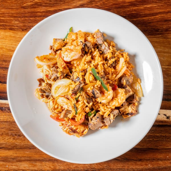 A white plate filled with shrimp and beef fried rice, garnished with onions and green peppers.
