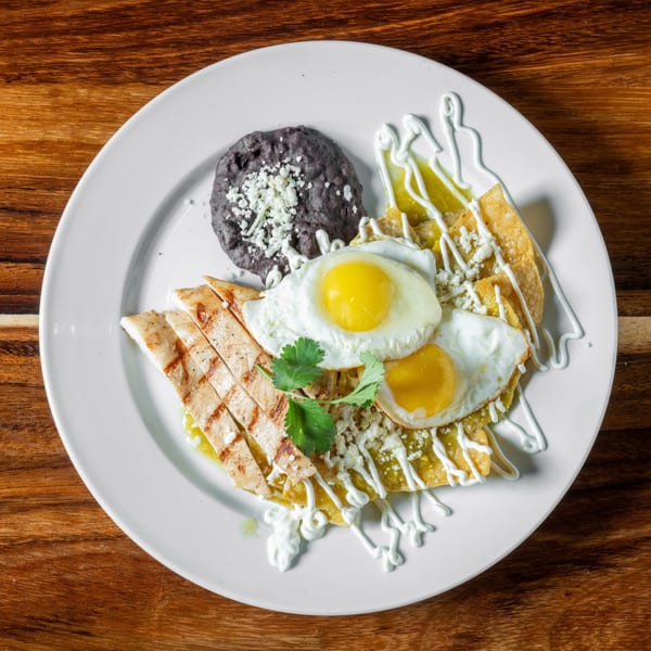 Chilaquiles with green salsa, two fried eggs, grilled chicken, black beans, and cilantro.